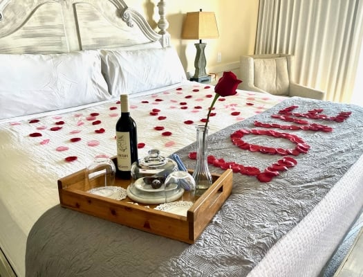 Rose pedals spelling love on king bed with tray of sweets and wine