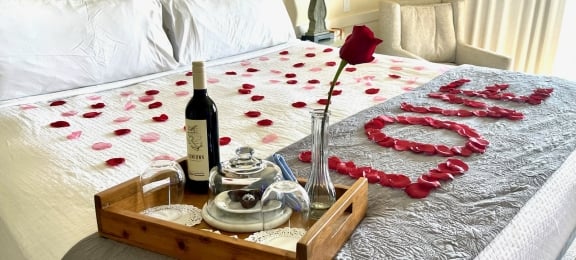 Rose pedals spelling love on king bed with tray of sweets and wine