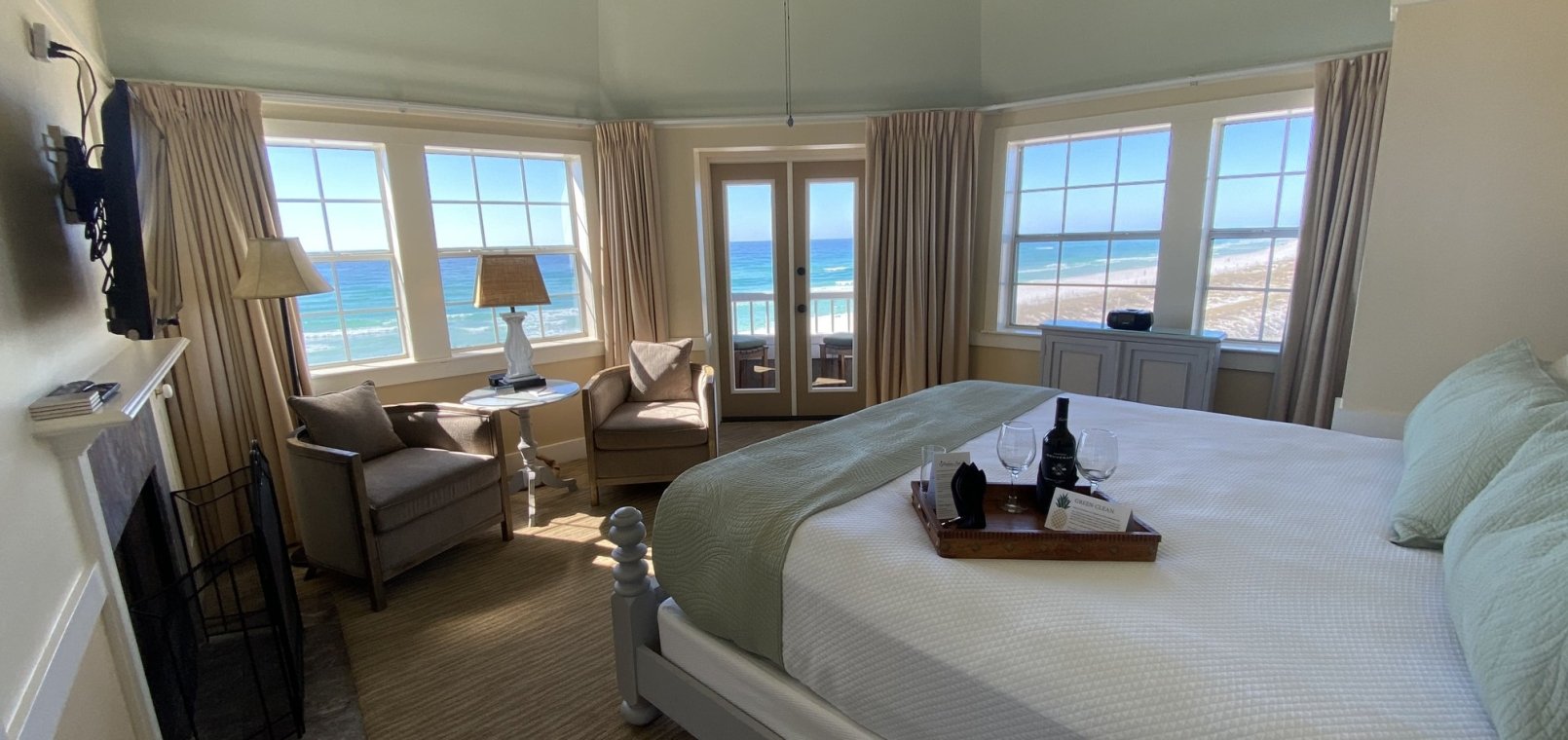 A king bed in a corner hotel suite with an ocean view