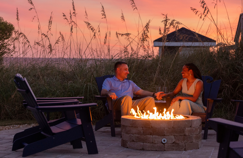 Couple at fire pit with a sunset backdrop