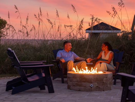 Couple at fire pit with a sunset backdrop